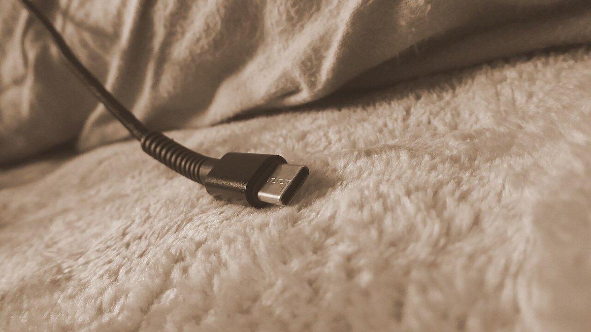 Kumaş bir yüzeyde duran, örgülü kılıflı bir USB-C şarj kablosunun ucu